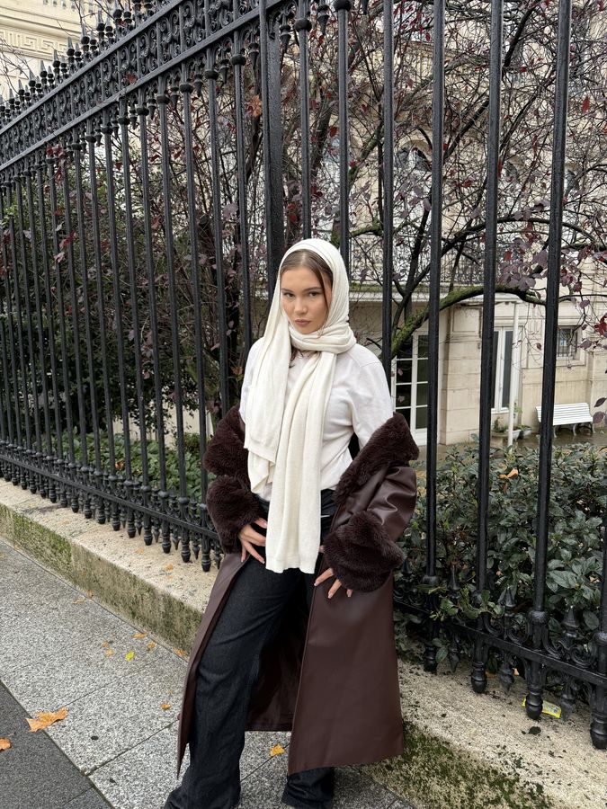 Kielo in a white headscarf and brown coat beside iron railings
